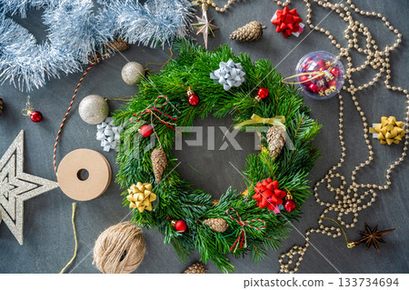 Top view of a fully decorated Christmas wreath surrounded by festive decor and crafting elements. A cozy handmade holiday creation made with care and creativity at home. Top view of a fully decorated Christmas wreath surrounded by festive decor and crafting elements. A cozy handmade holiday creation made with care and creativity at home. 133734694