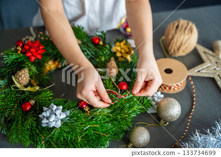 Close-up of small hands holding a decorated Christmas wreath during a holiday craft activity. A symbolic moment of festive creativity and childhood involvement in home traditions. Close-up of small hands holding a decorated Christmas wreath during a holiday craft activity. A symbolic moment of festive creativity and childhood involvement in home traditions. 133734699