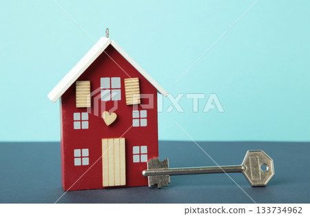 Wooden house model with key on blue background. Mortgage loan for buying home or real estate property, money saving plan, money risk management in financial banking concept. 133734962