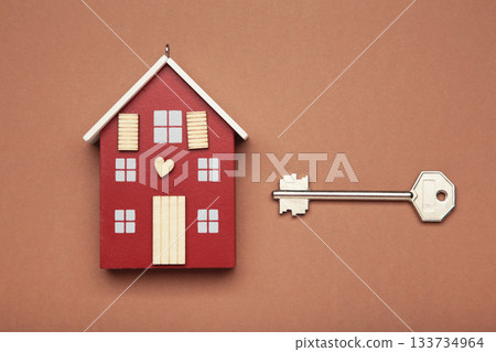 Wooden house model with key on brown background. Mortgage loan for buying home or real estate property, money saving plan, money risk management in financial banking concept. Wooden house model with key on brown background. Mortgage loan for buying home or real estate property, money saving plan, money risk management in financial banking concept. 133734964