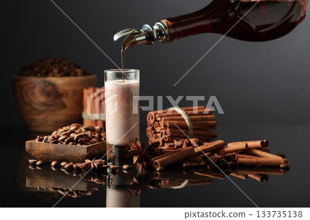 Coffee liquor is poured from a bottle into a glass with cream. 133735138