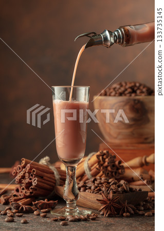 Irish cream and coffee liquor is poured from a bottle into a glass. Irish cream and coffee liquor is poured from a bottle into a glass. 133735145