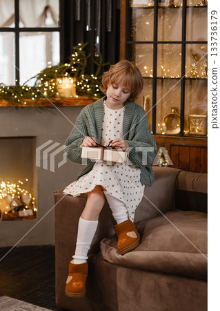 Caucasian girl opening gift box in cozy Christmas room with warm lights and wooden decor Caucasian girl opening gift box in cozy Christmas room with warm lights and wooden decor 133736179