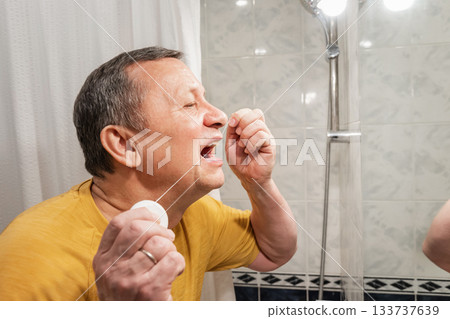 Using dental floss for interdental cleaning, caucasian adult male performing oral hygiene routine at bathroom mirror. Man Brushing Teeth Using dental floss for interdental cleaning, caucasian adult male performing oral hygiene routine at bathroom mirror. Man Brushing Teeth 133737639