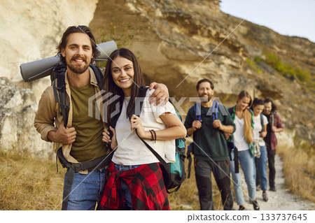 Friends tourists standing outdoor having walking tour of the mountains and looking at camera. 133737645