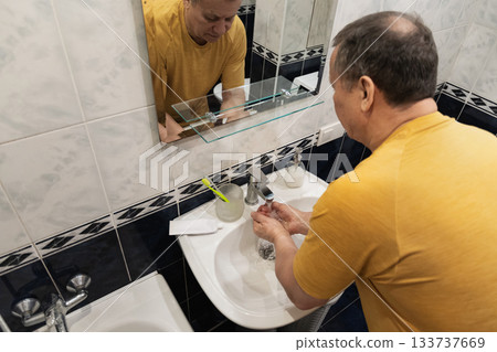 Washing hands under running water before brushing teeth, caucasian adult male preparing for oral hygiene at home sink. Man Brushing Teeth Washing hands under running water before brushing teeth, caucasian adult male preparing for oral hygiene at home sink. Man Brushing Teeth 133737669