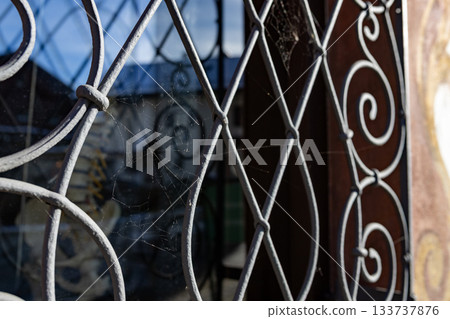 A close-up view of an old metal window grille with delicate spider webs catching the sunlight, creating a rustic and atmospheric detail of decay, texture, and quiet stillness. 133737876
