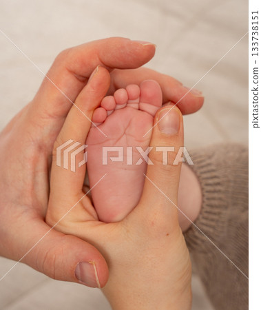 Close-up of two adult hands gently surrounding a babys tiny foot. The soft tones and natural textures emphasize warmth, family unity and early bonding, suitable for parenting, love and newborn care 133738151