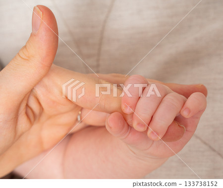 A babys tiny hand gripping an adults thumb. The warm tones and soft textures create an intimate, emotional portrait symbolizing trust, connection and early bonding between parent and child. 133738152