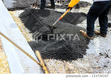 Workers laying asphalt for road construction with shovels on suburban area Workers laying asphalt for road construction with shovels on suburban area 133738197