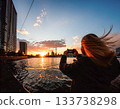 一位長髮女子正在用智慧型手機拍攝城市日落。 133738298