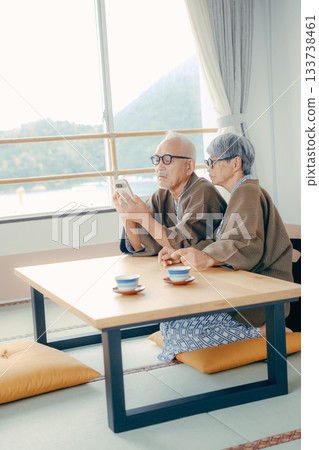 An elderly couple looking at a smartphone together in a Japanese-style room at a ryokan 133738461