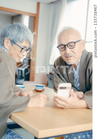 一對老年夫婦在日式旅館的房間裡一起看智慧型手機。 133738467