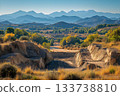 Open quarry site surrounded by autumn trees and layered mountain ranges under clear blue sky 133738810