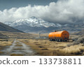Orange tanker trailer resting in a wide valley with snowy mountains under dramatic clouds 133738811