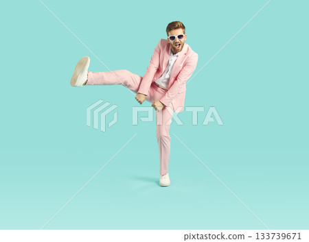 Happy, funny, cheerful young man in a pink suit dancing on a blue studio background Happy, funny, cheerful young man in a pink suit dancing on a blue studio background 133739671
