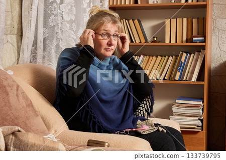 Using reading glasses for presbyopia woman over 50 puts on glasses when sits down to needlework at home. 133739795