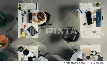 Top down view of work team engaged in negotiation consulting during business meeting. Employees use laptops to analyze finance data and performance reports in office. Top down view of work team engaged in negotiation consulting during business meeting. Employees use laptops to analyze finance data and performance reports in office. 133740382
