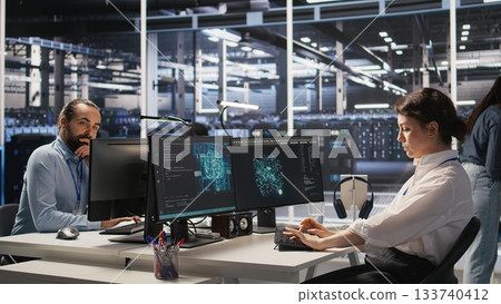 Tired data center engineer stretching, monitoring server clusters performing AI training. Fatigued server farm IT specialist supervising computing systems managing deep learning operations, camera A 133740412