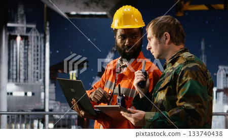 Soldier in uniform operate communication devices during a maritime mission with engineer, providing security for offshore platform logistics and drilling rig protection operations. 133740438