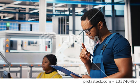 Portrait of engineer in photovoltaics factory reviewing paperwork to diagnose malfunctioning systems. Solar panels plant worker reading inspection data files to reduce downtime. Camera B. Portrait of engineer in photovoltaics factory reviewing paperwork to diagnose malfunctioning systems. Solar panels plant worker reading inspection data files to reduce downtime. Camera B. 133740486