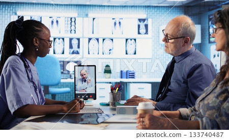 Nurse discussing with patients while on videocall with an expert, receiving professional diagnosis and different advice for recovery. Doctor supporting clients via internet conference. Camera A. Nurse discussing with patients while on videocall with an expert, receiving professional diagnosis and different advice for recovery. Doctor supporting clients via internet conference. Camera A. 133740487