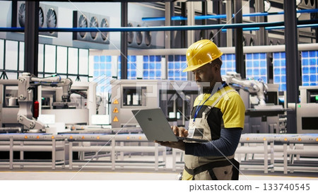 Industry 4.0 plant engineer following maintenance procedures to mend bugs. Smart factory professional analyzing data on laptop to predict production lines and robotic arms failures, camera A 133740545