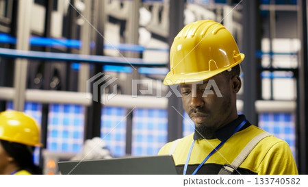 Industry 4.0 plant engineer following maintenance procedures to mend bugs. Smart factory professional analyzing data on laptop to predict production lines and robotic arms failures, camera B Industry 4.0 plant engineer following maintenance procedures to mend bugs. Smart factory professional analyzing data on laptop to predict production lines and robotic arms failures, camera B 133740582