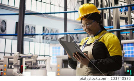 Smiling engineer in smart factory performing predictive maintenance using tablet, analyzing IoT sensor data. Industrial plant worker managing operational reliability of photovoltaic systems, camera A 133740583