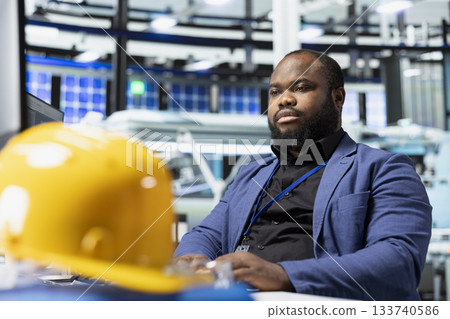 Male factory consultant observes production systems on a pc in a solar plant, providing expert feedback on efficiency, safety and sustainability aligned with green energy initiatives. 133740586