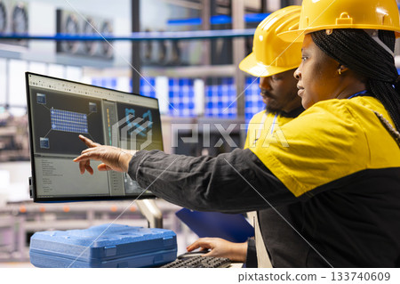 Smart factory technicians utilizing computer to enhance solar energy efficiency in industrial plant. Industry 4.0 experts supervise automated machinery involved in solar panel production. 133740609