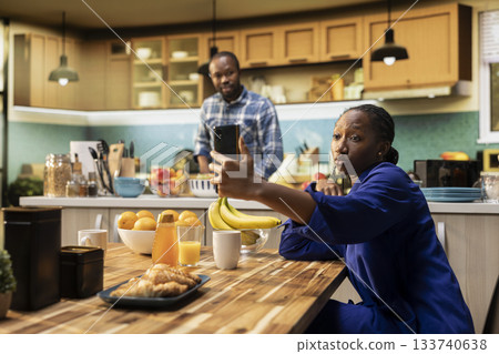 African american woman takes selfies on her smartphone and acting silly, boyfriend laughing at her and enjoying a cute funny moment together on a weekend morning. Relaxation at home. African american woman takes selfies on her smartphone and acting silly, boyfriend laughing at her and enjoying a cute funny moment together on a weekend morning. Relaxation at home. 133740638