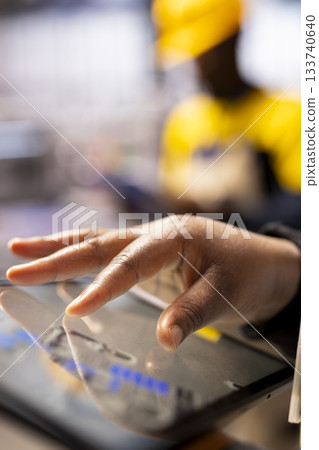 Closeup of technician leveraging a digital app to enhance solar energy output. Selective focus on factory specialist using tablet, supervising smart machinery used in solar panel production. Closeup of technician leveraging a digital app to enhance solar energy output. Selective focus on factory specialist using tablet, supervising smart machinery used in solar panel production. 133740640