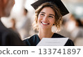 Young female graduate in academic dress smiles brightly while receiving diploma during graduation ceremony, celebrating a significant educational achievement 133741897