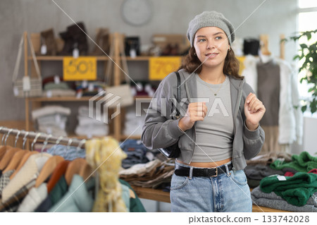 Positive young woman trying winter hat in clothing store Positive young woman trying winter hat in clothing store 133742028