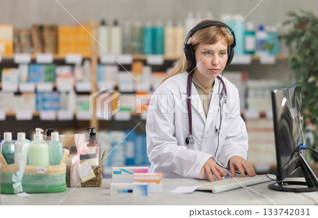 Female pharmacist with headphones working with computer in drugstore 133742031