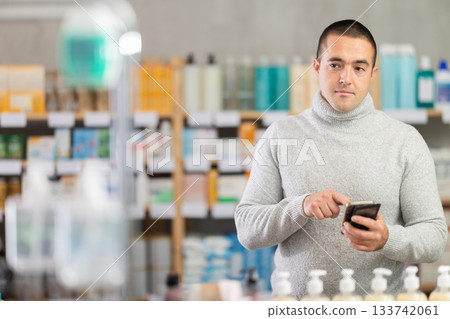 Male shopper searches for necessary goods on shelves of a supermarket, checking the list on her smartphone Male shopper searches for necessary goods on shelves of a supermarket, checking the list on her smartphone 133742061