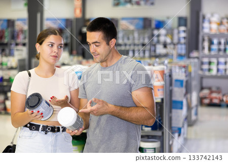 Interested couple talking and selecting paints in building supplies store 133742143