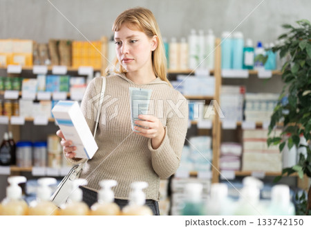 Girl in autumn clothes choosing skin cream at drugstore 133742150