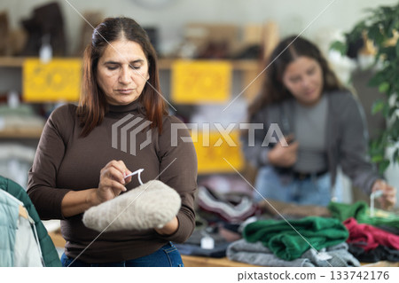 Latina woman chooses demi-season hat in clothing store. 133742176