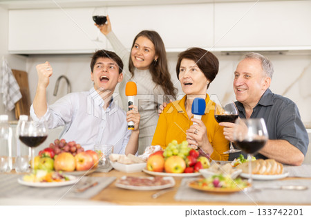 Laughing family singing together, parents and adult children having party singing song using microphone at home 133742201