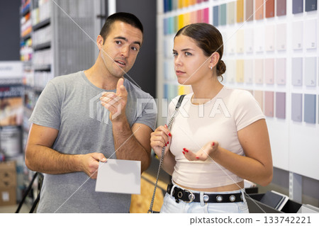 Near stand with samples paint, palette of colors of coating, couple examines showcase 133742221