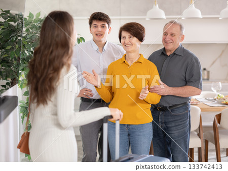Happy young girl coming to meet boyfriend's family. Elderly mother, father and young guy joyfully greeting at door Happy young girl coming to meet boyfriend's family. Elderly mother, father and young guy joyfully greeting at door 133742413