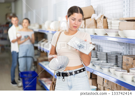 Young female shopper choosing ceramic plates at Asian store Young female shopper choosing ceramic plates at Asian store 133742414