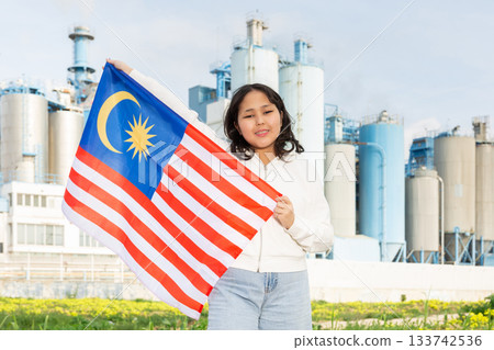 Happy young woman with flag of Malaysia against background of factory 133742536