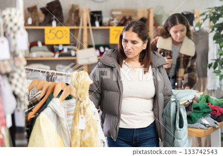 Female shopper selects some fall winter outerwear at clothing store Female shopper selects some fall winter outerwear at clothing store 133742543