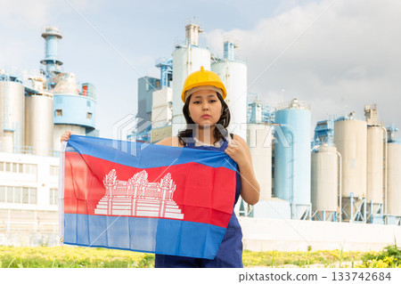 Sad young woman in helmet holding flag of Cambodia against background of factory Sad young woman in helmet holding flag of Cambodia against background of factory 133742684