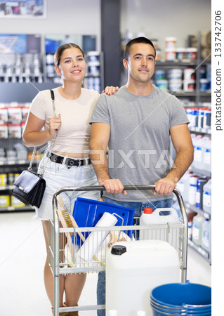 Interested couple pushing shopping trolley with purchases in construction hypermarket Interested couple pushing shopping trolley with purchases in construction hypermarket 133742706
