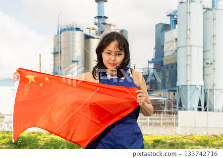 Portrait of teenage girl in blue overalls with flag of China in her hands against the backdrop of modern metallurgical plant Portrait of teenage girl in blue overalls with flag of China in her hands against the backdrop of modern metallurgical plant 133742716