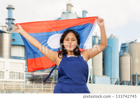 Young girl in blue overalls waving the flag of Laos against backdrop of modern metallurgical plant Young girl in blue overalls waving the flag of Laos against backdrop of modern metallurgical plant 133742745